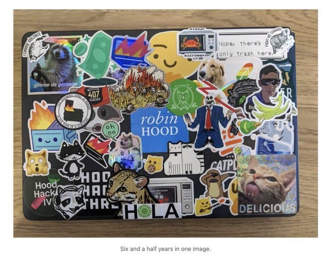 A Robinhood employee laptop covered in office stickers, including a raccoon sticker reading gimme da gorbage